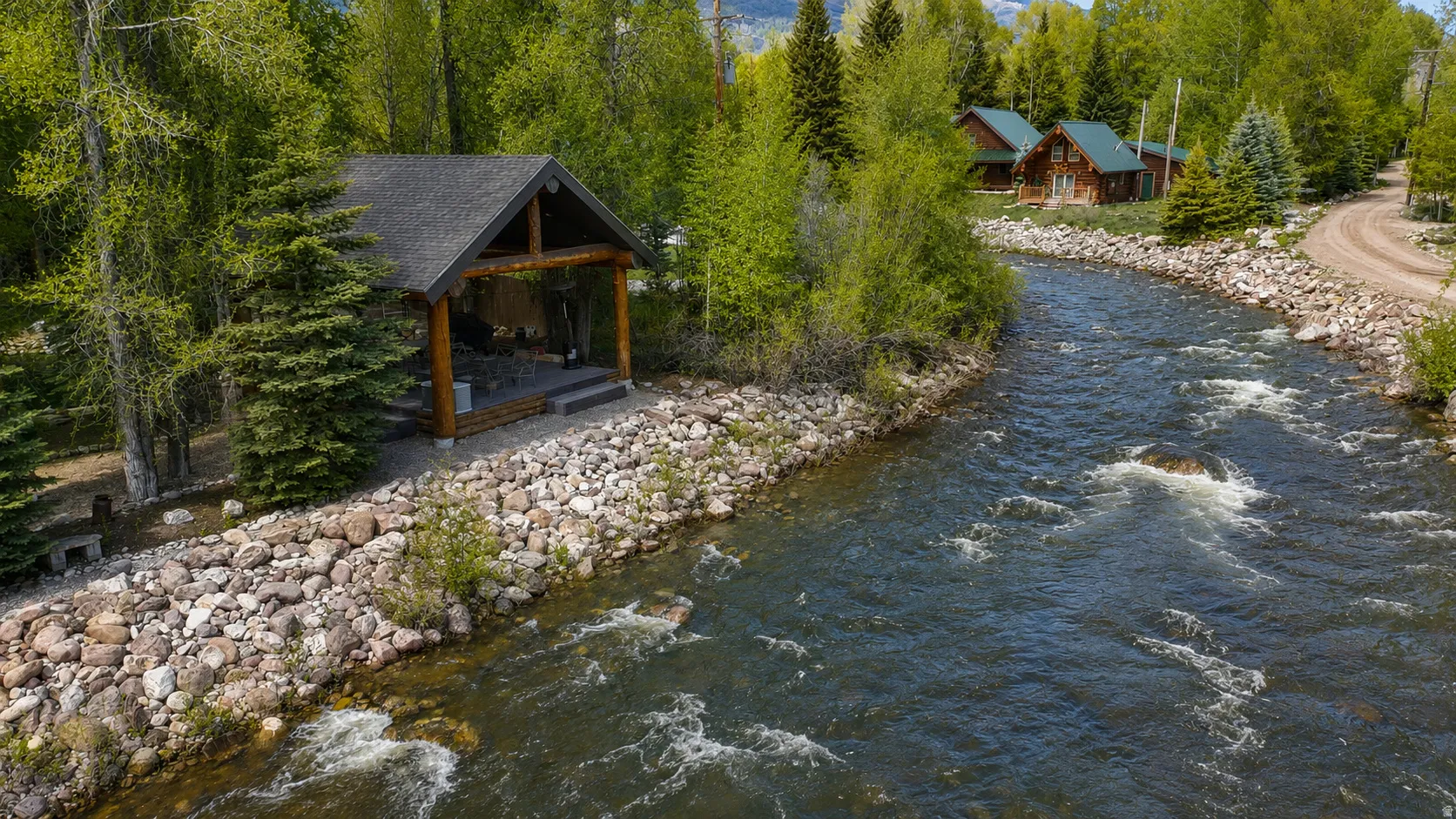 Riverfront pavilion featuring exposed timber beams, a covered patio, and a stone-lined bank