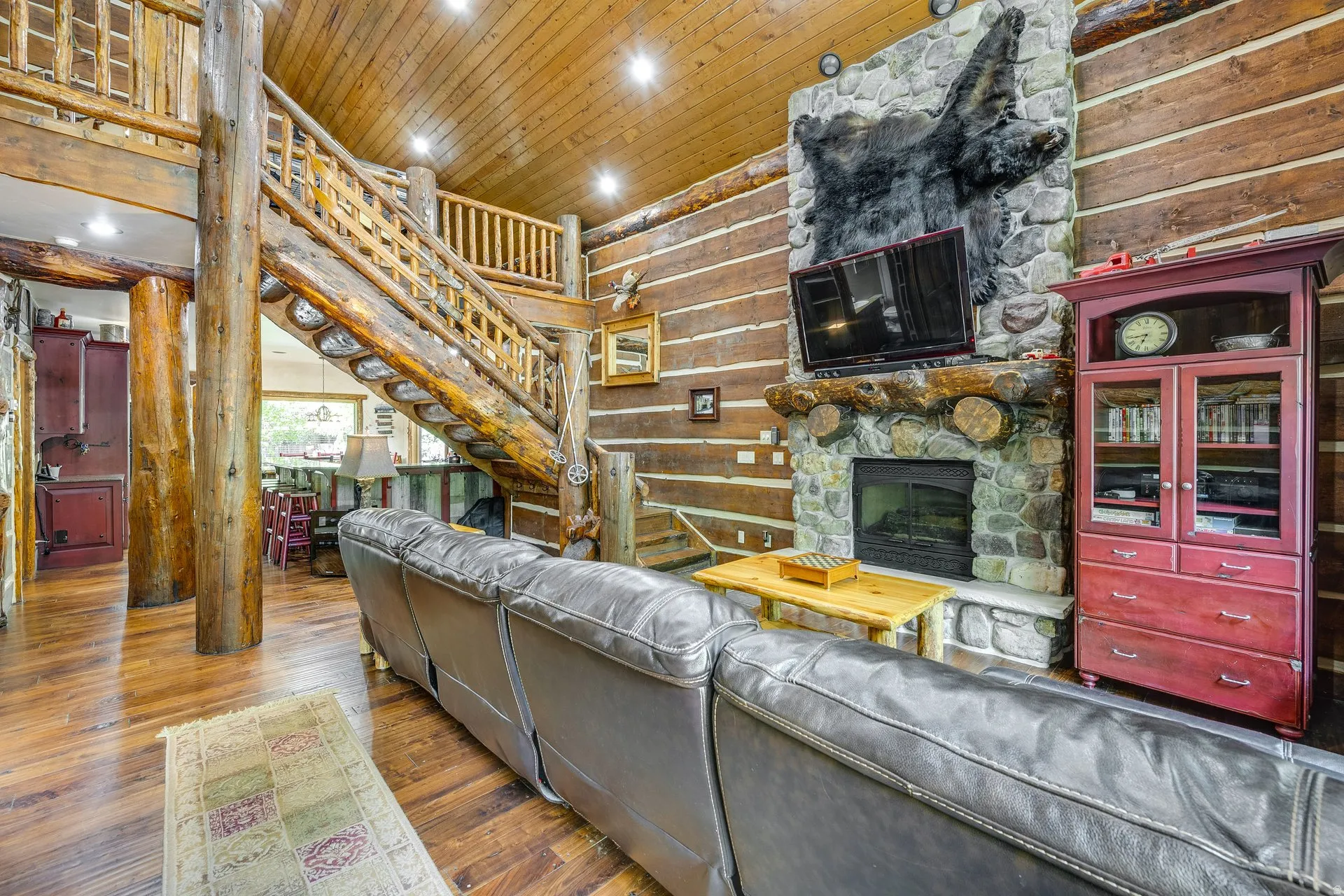 Expansive living area with wood-finish flooring, a stone fireplace, and log walls