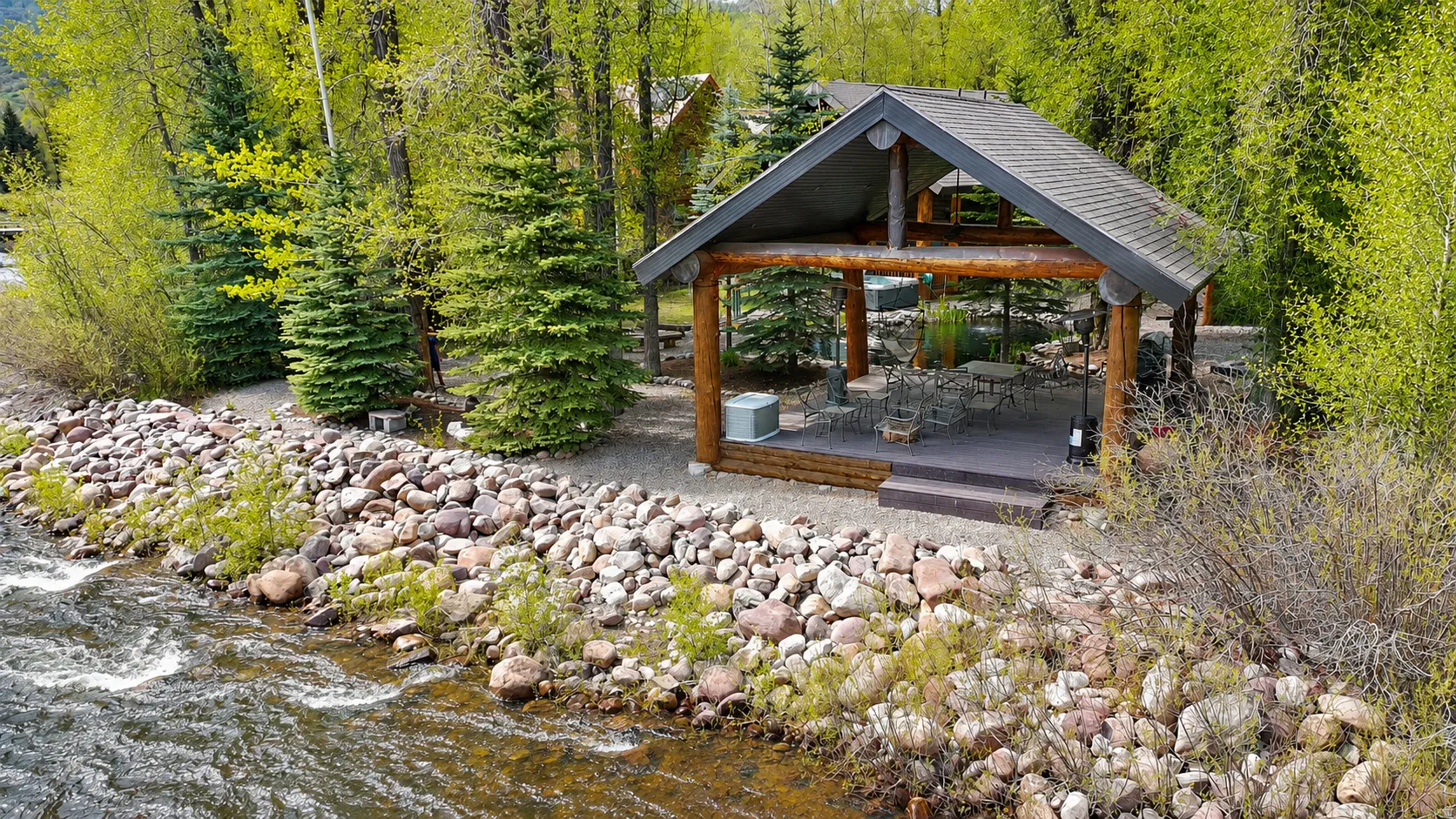 Riverside covered patio with exposed log beams, recessed lighting, and a composite deck