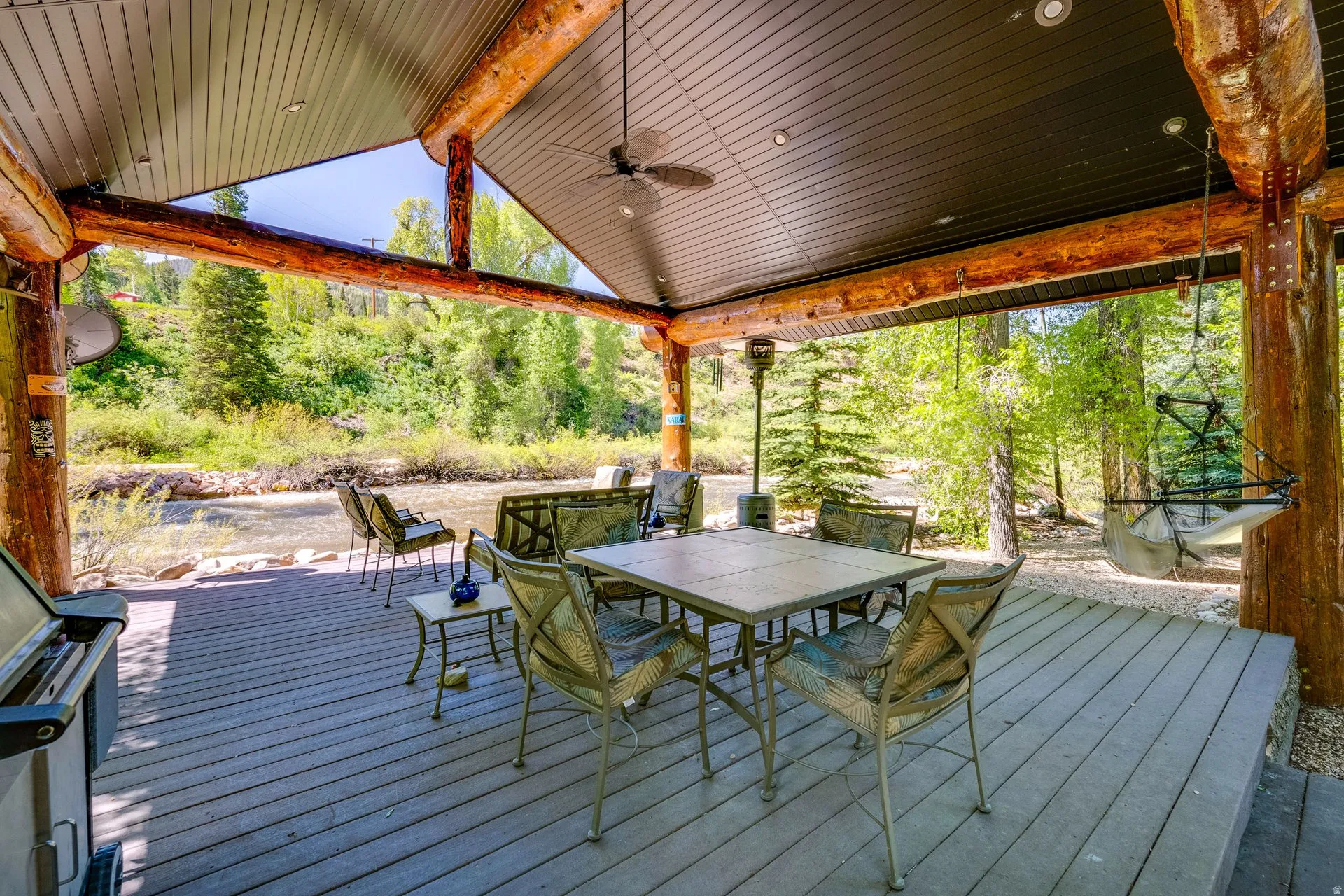 Expansive covered deck featuring a wood-finish floor, natural log support beams, recessed lighting, and a ceiling fan