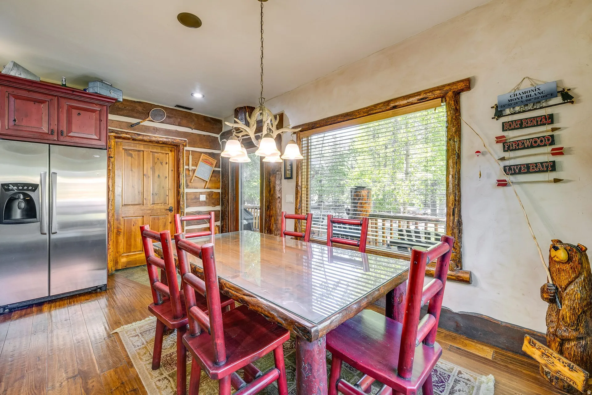 Dining area featuring a wood-finish table with a glass top, a large window, a rustic chandelier, wood-finish flooring, and a stainless steel refrigerator