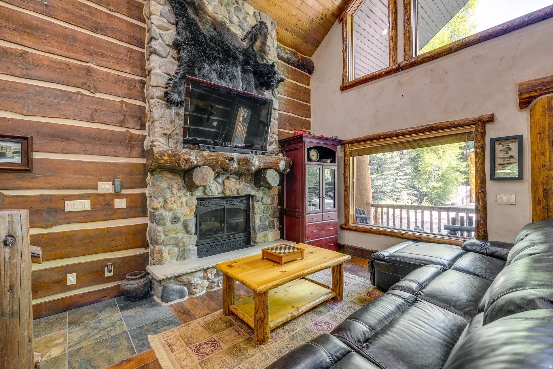 Stone fireplace with a hearth, log walls, and wood-finish flooring