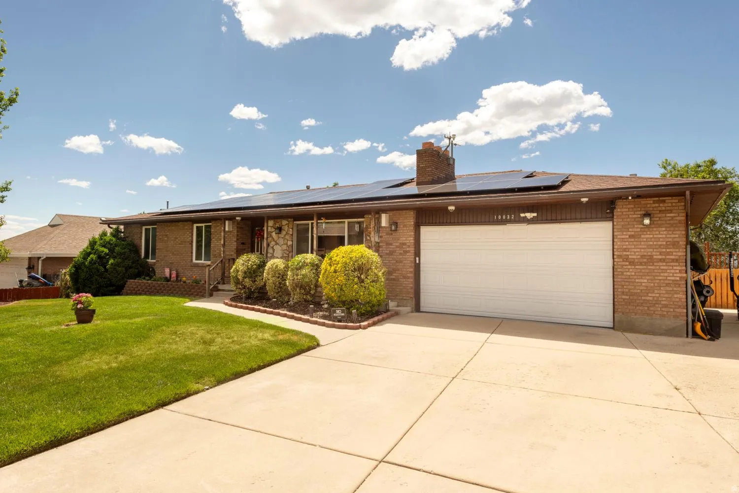 Brick and stone facade residence featuring a concrete driveway, attached garage, solar panel system, and manicured front lawn