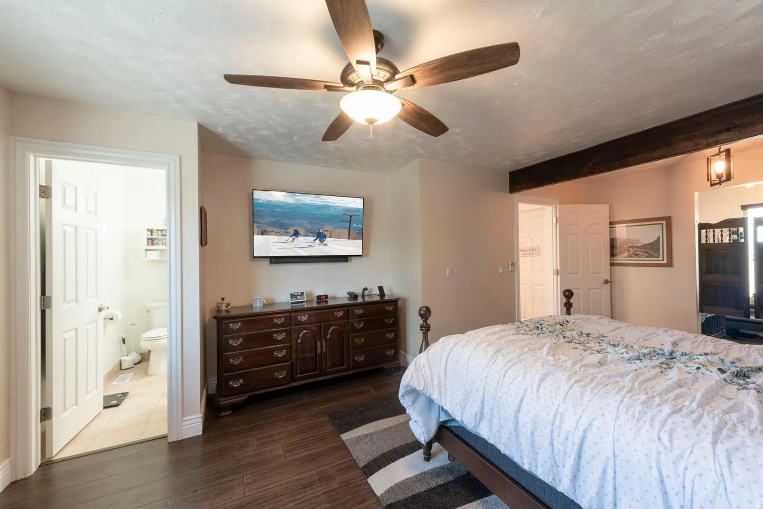 Spacious bedroom featuring wood-finish flooring, a ceiling fan, and exposed wood beam accents