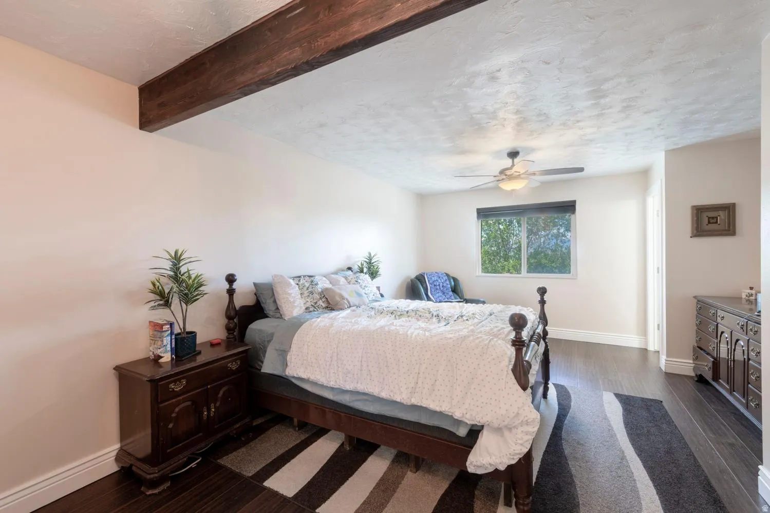 Bedroom featuring dark wood-finish flooring, a wood ceiling beam, textured ceiling, and a ceiling fan with integrated lighting