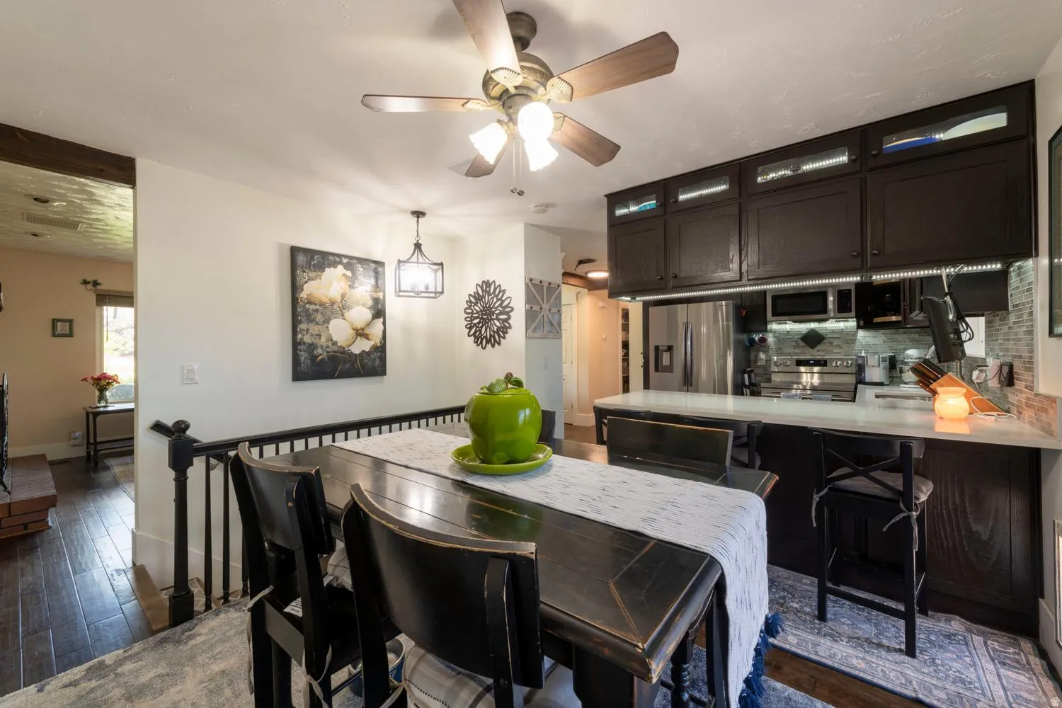 Dining area featuring wood-finish flooring, a black railing, and an overhead ceiling fan with lighting