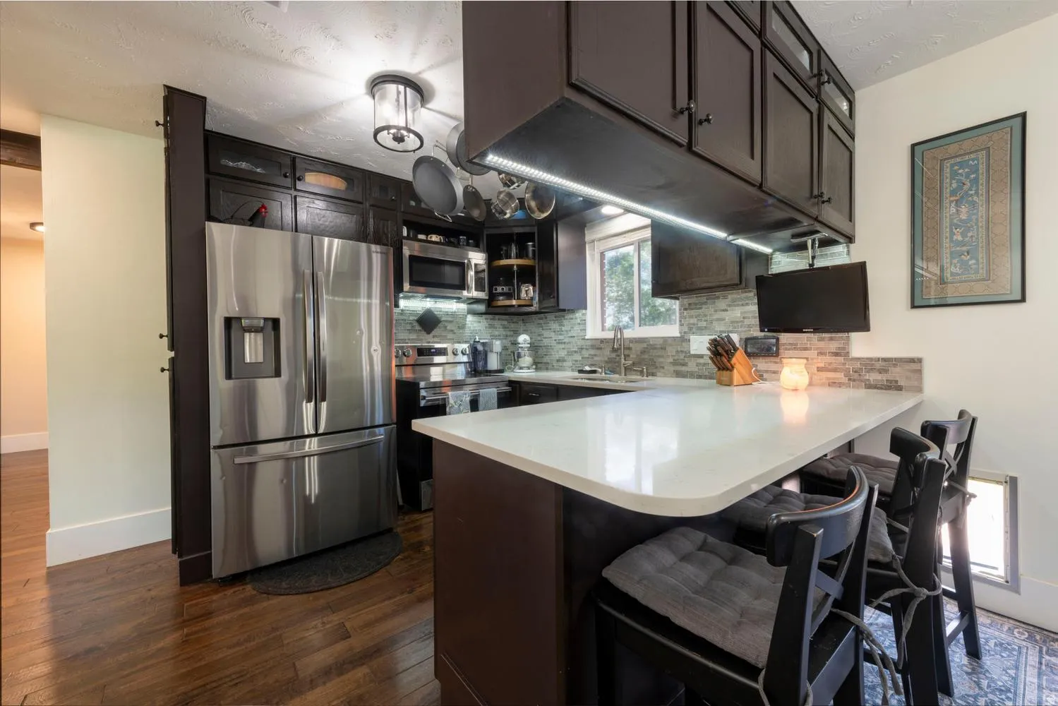 Modern kitchen featuring dark cabinetry, stainless steel appliances, a breakfast bar with a light-toned countertop, and wood-finish flooring