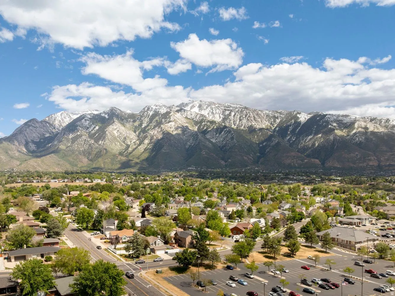Expansive mountain range backdrop framing a residential area with mature trees and a commercial parking lot