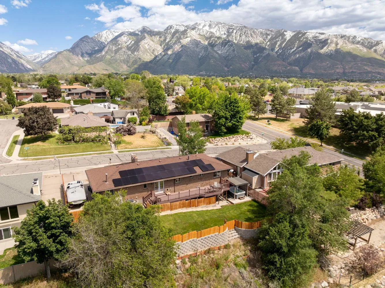 Brick exterior residence featuring a brown shingled roof with solar panels, a multi-level wood deck, and a fenced backyard with terraced landscaping
