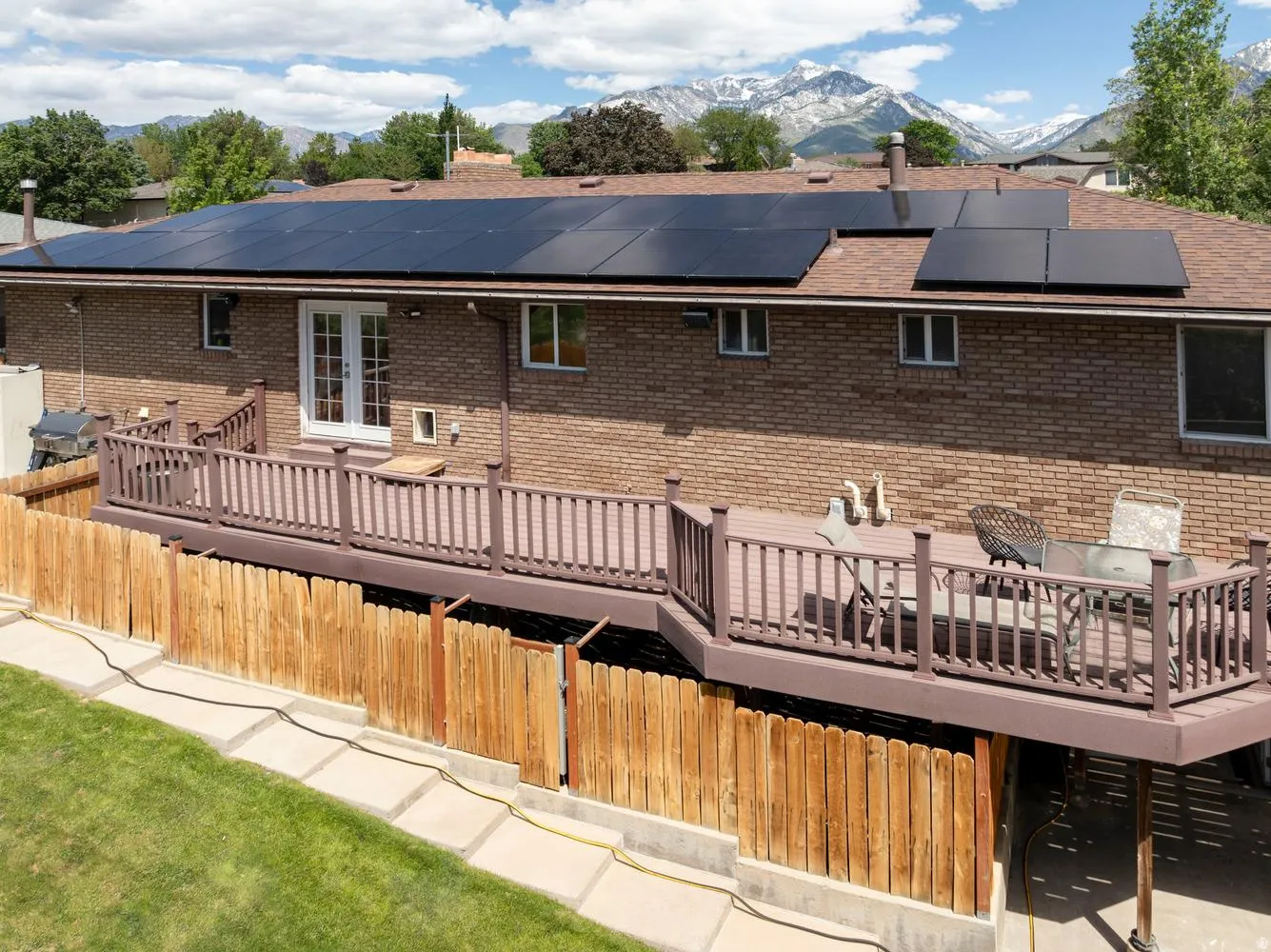 Brick exterior featuring a spacious elevated deck with railing, double French doors, and solar panels on the roof