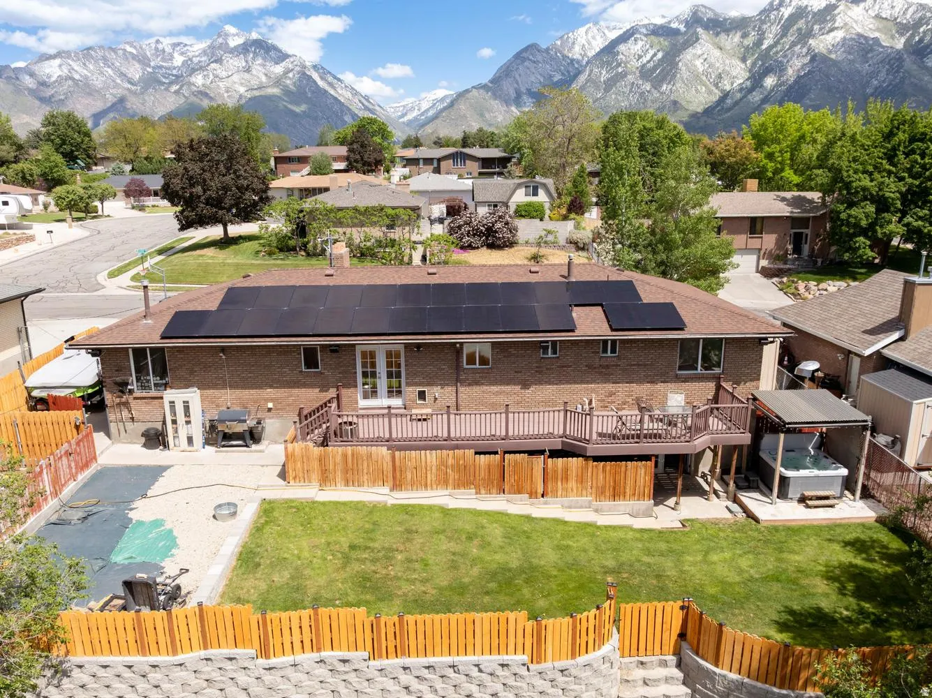 Rear brick exterior featuring a multi-level wood deck, ground-level hot tub with a covered pergola, and an expansive lawn