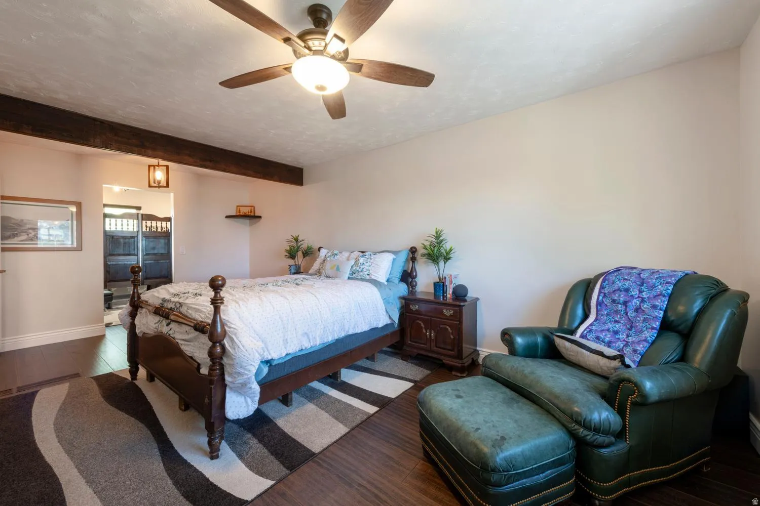 Spacious room featuring wood-finish flooring, a ceiling fan with integrated lighting, and exposed ceiling beams