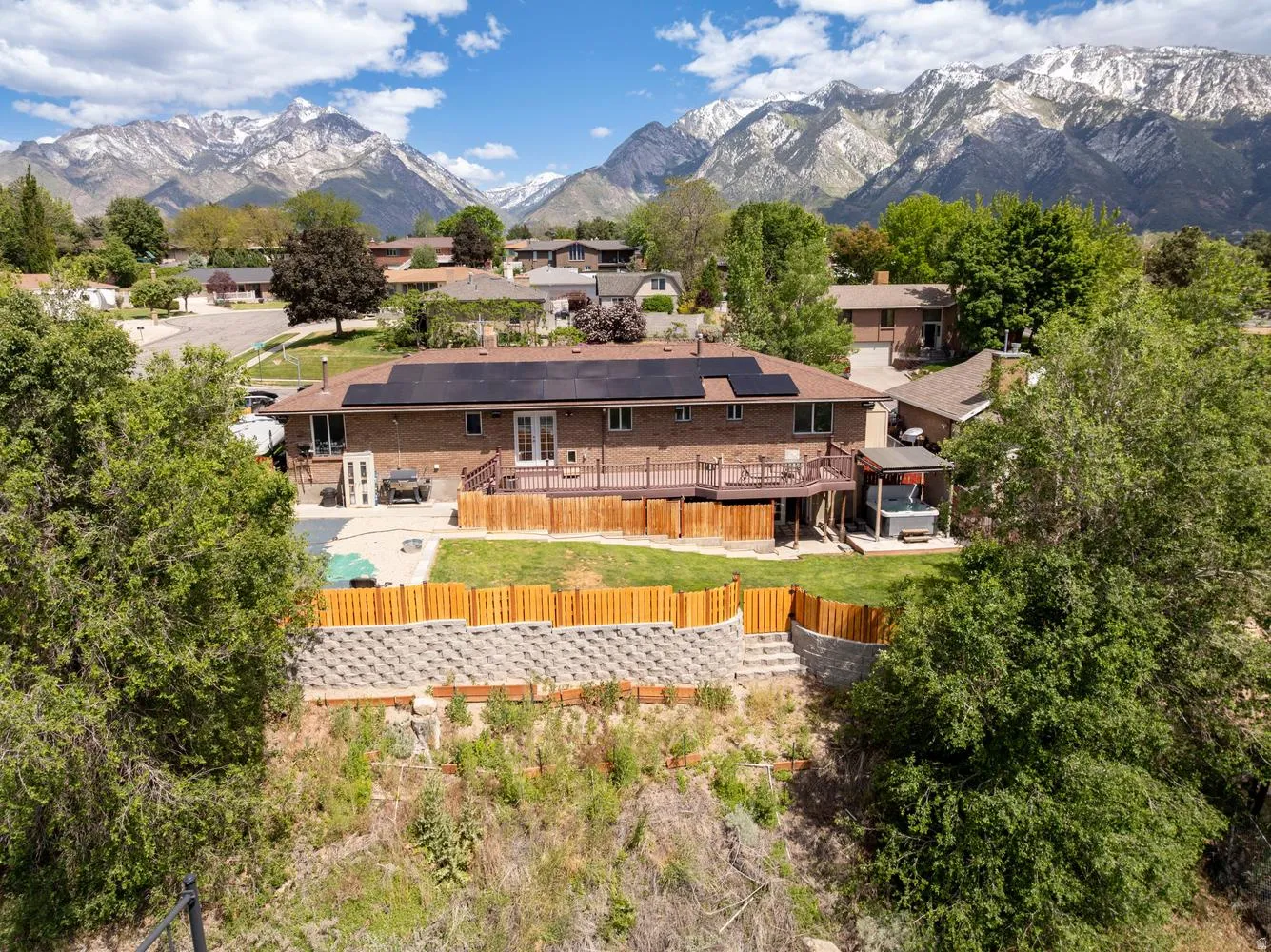 Brick exterior property featuring a spacious wood deck, solar panels, and a fenced backyard with a lawn