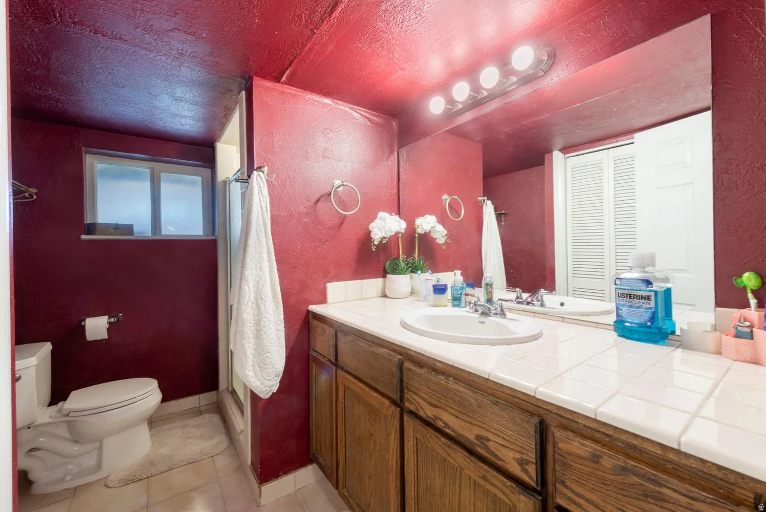 Bathroom featuring a wood-finish vanity with a tile countertop, an oval undermount sink, and a large wall-mounted mirror