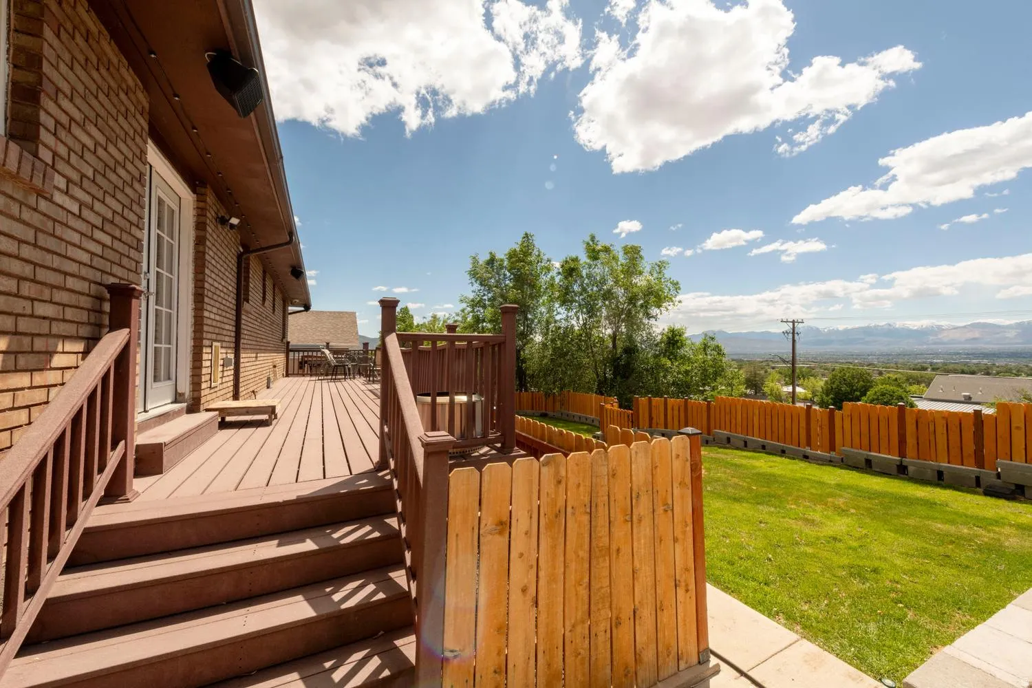 Rear exterior featuring a brick facade, multi-level composite deck, and a fenced backyard with green lawn