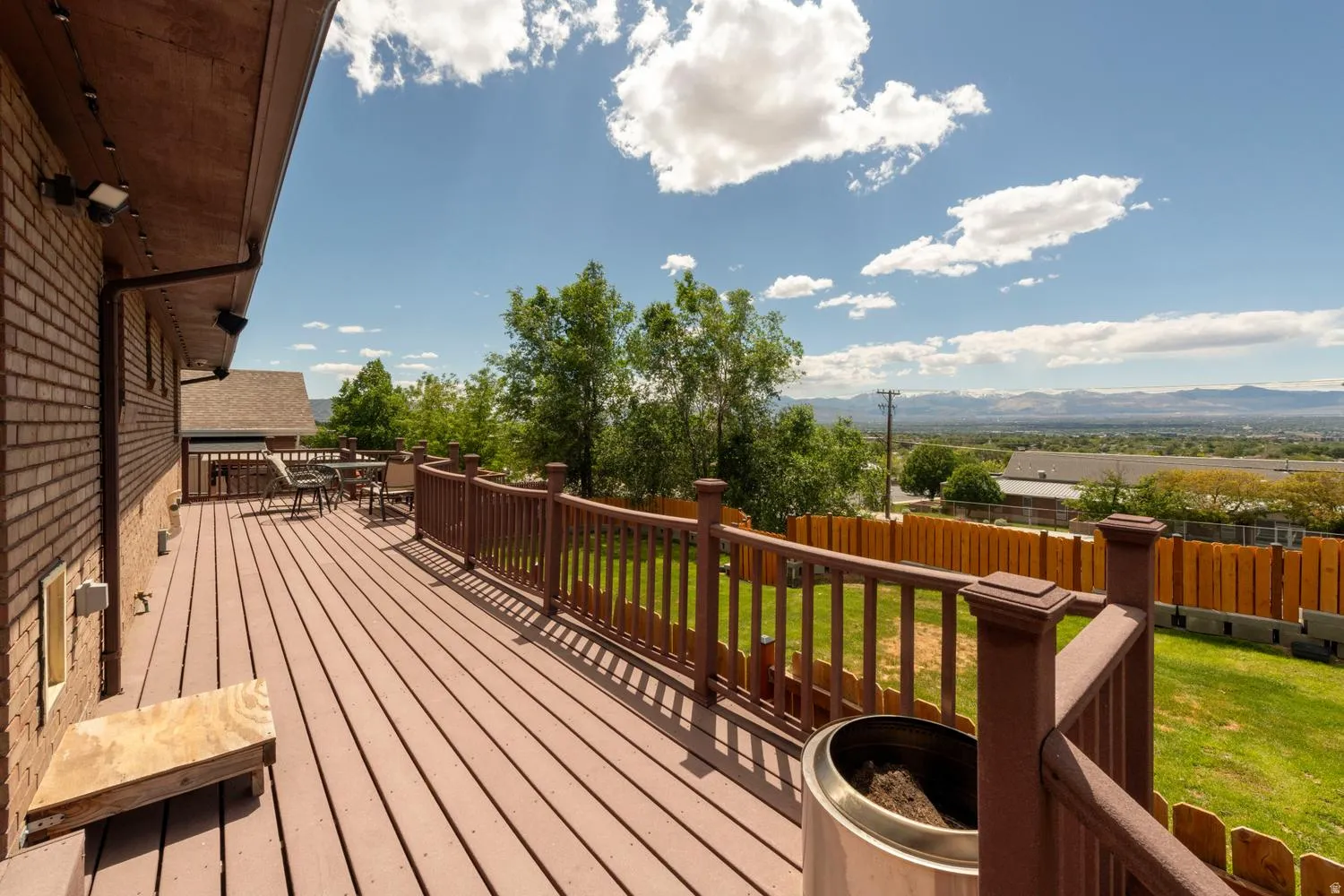 Spacious outdoor deck with protective railing, brick exterior, and distant mountain backdrop