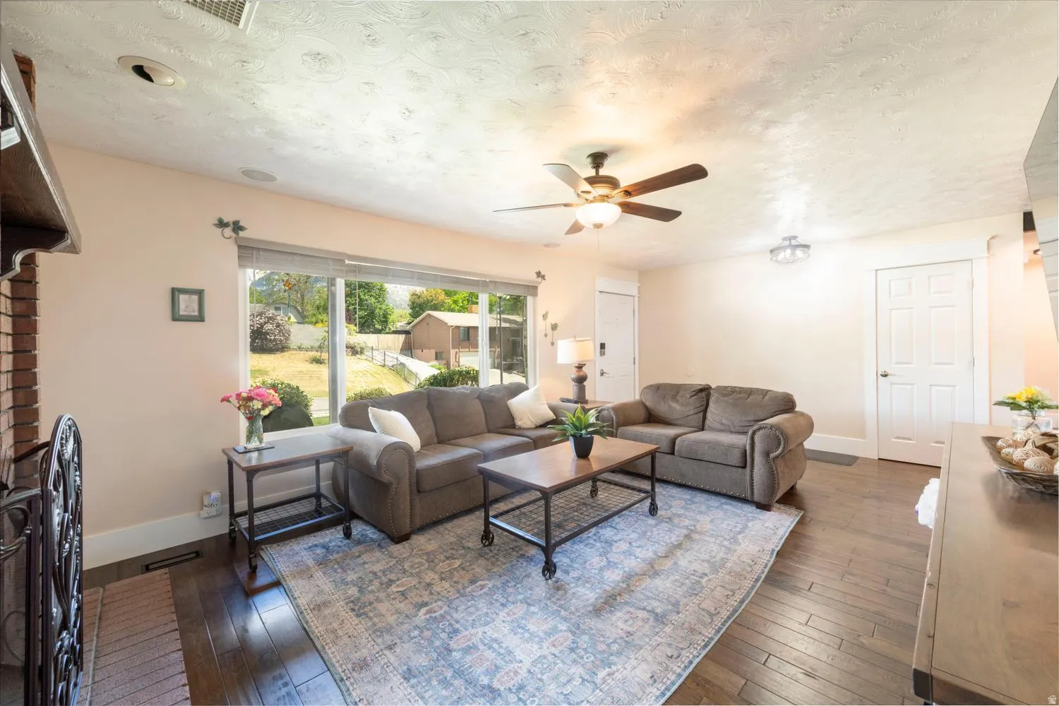 Spacious living area featuring large picture windows, dark wood-finish flooring, and a ceiling fan