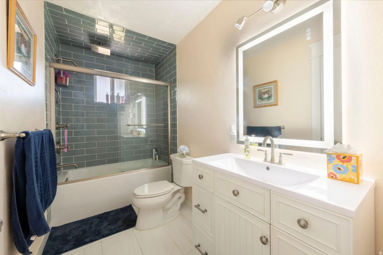 Bathroom featuring an illuminated vanity mirror, white vanity with storage, integrated sink, and brushed nickel fixtures