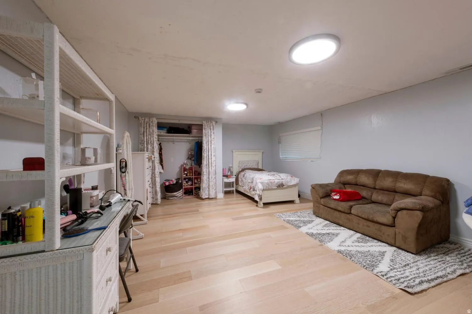 Spacious room featuring light wood-finish flooring, two round ceiling lights, and an open closet area