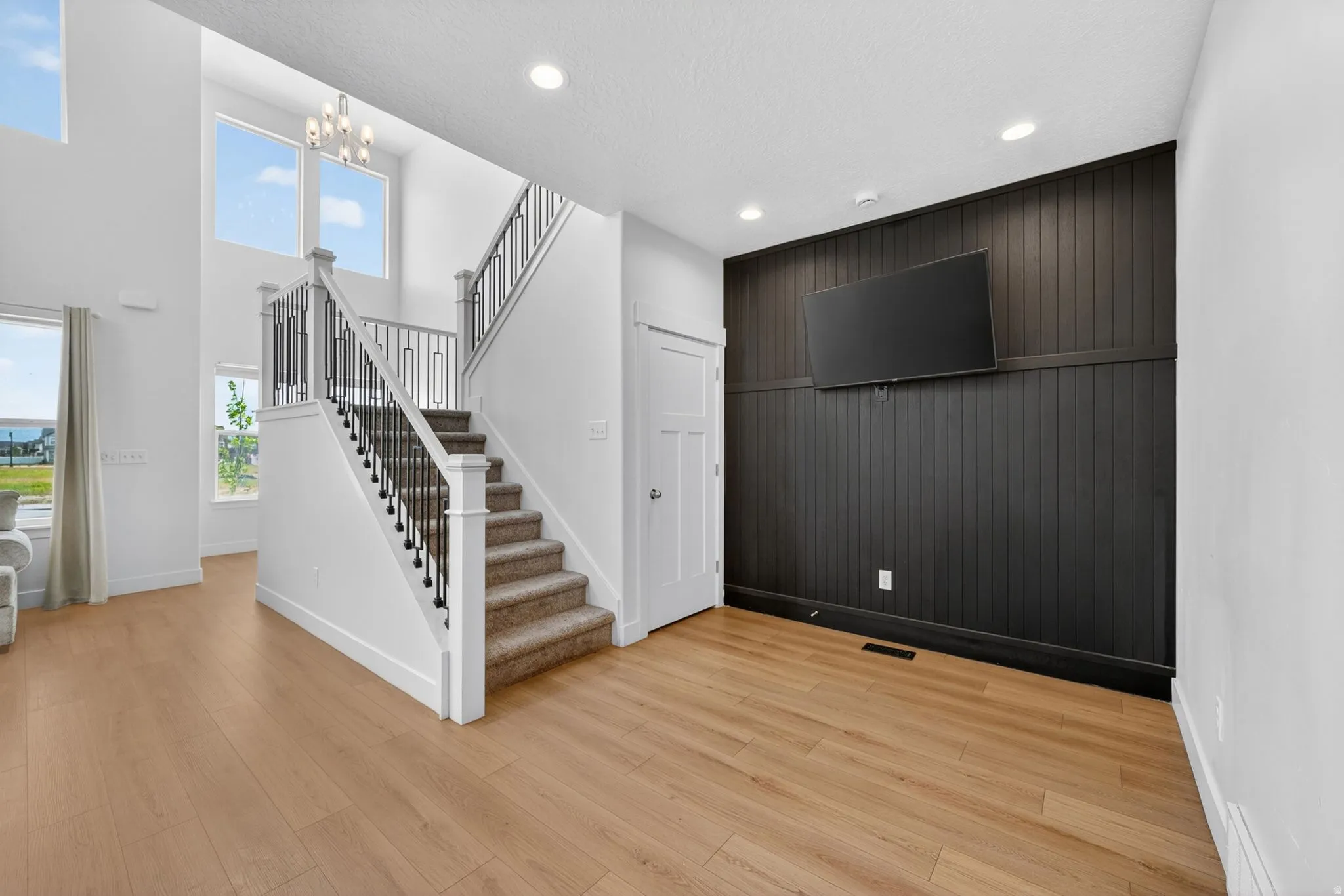 Two-story entry featuring light wood-finish flooring, a carpeted staircase with white risers and dark metal balusters, and a modern chandelier