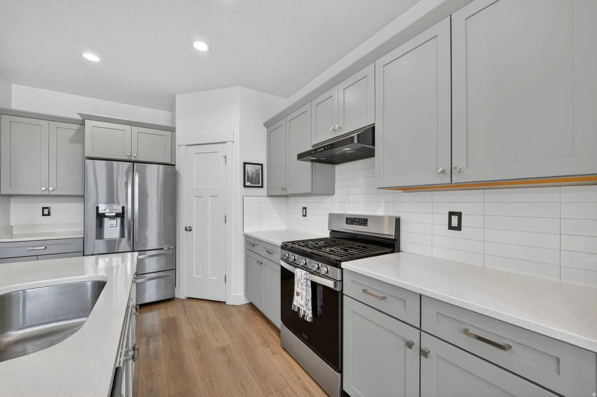 Modern kitchen featuring light gray cabinetry, stainless steel appliances, white subway tile backsplash, and light-toned wood-finish flooring