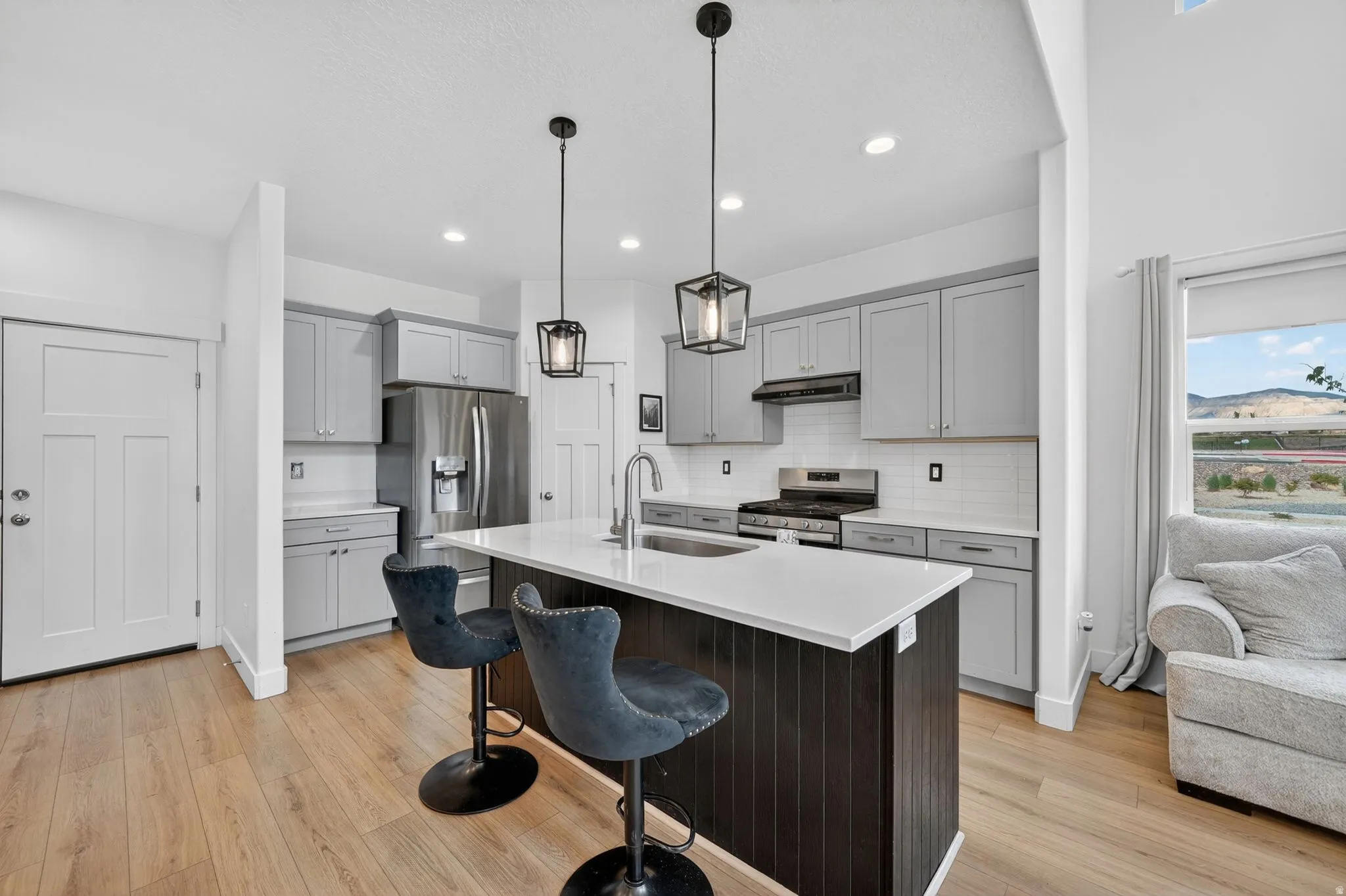 Modern kitchen featuring a central island with a waterfall countertop, pendant lighting, and light wood-finish flooring