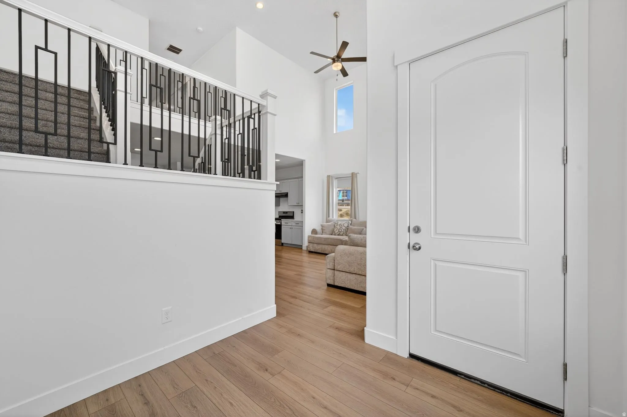 Entryway featuring a paneled front door with an arched top panel, wood-finish flooring, a contemporary black metal stair railing, high vaulted ceilings, and recessed lighting