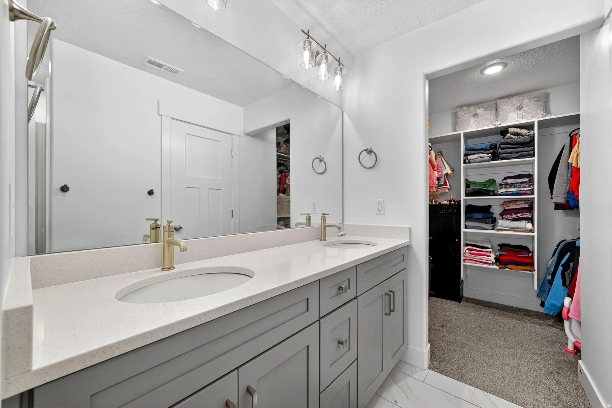Double vanity with light gray cabinetry, light-colored countertops, and gold-finish faucets