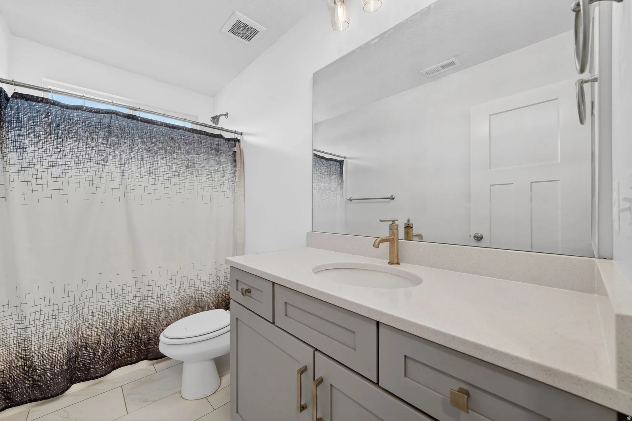 Bathroom vanity with light gray shaker cabinetry, gold-finish hardware, and a white countertop