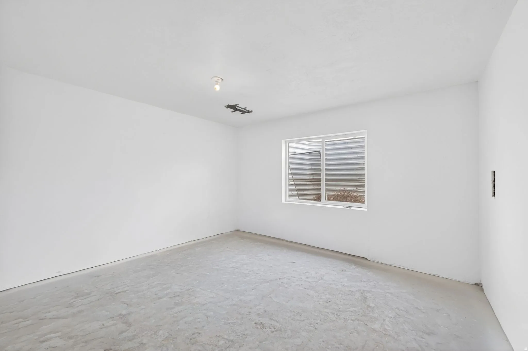 Unfinished room featuring white walls, concrete flooring, and a single window with a window well