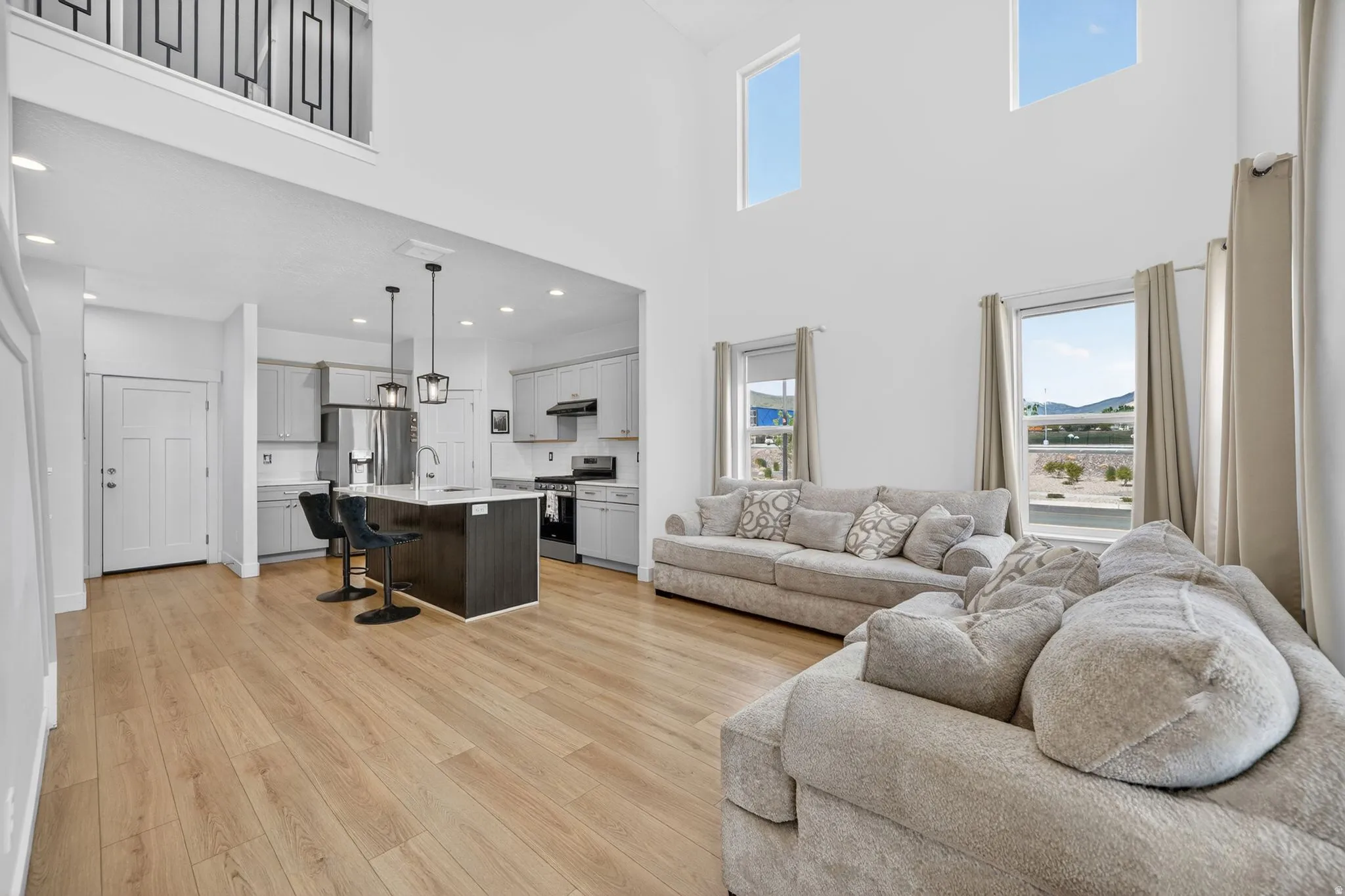 Open-concept living space featuring high ceilings with upper windows, wood-finish flooring, and a kitchen with an island and stainless steel appliances