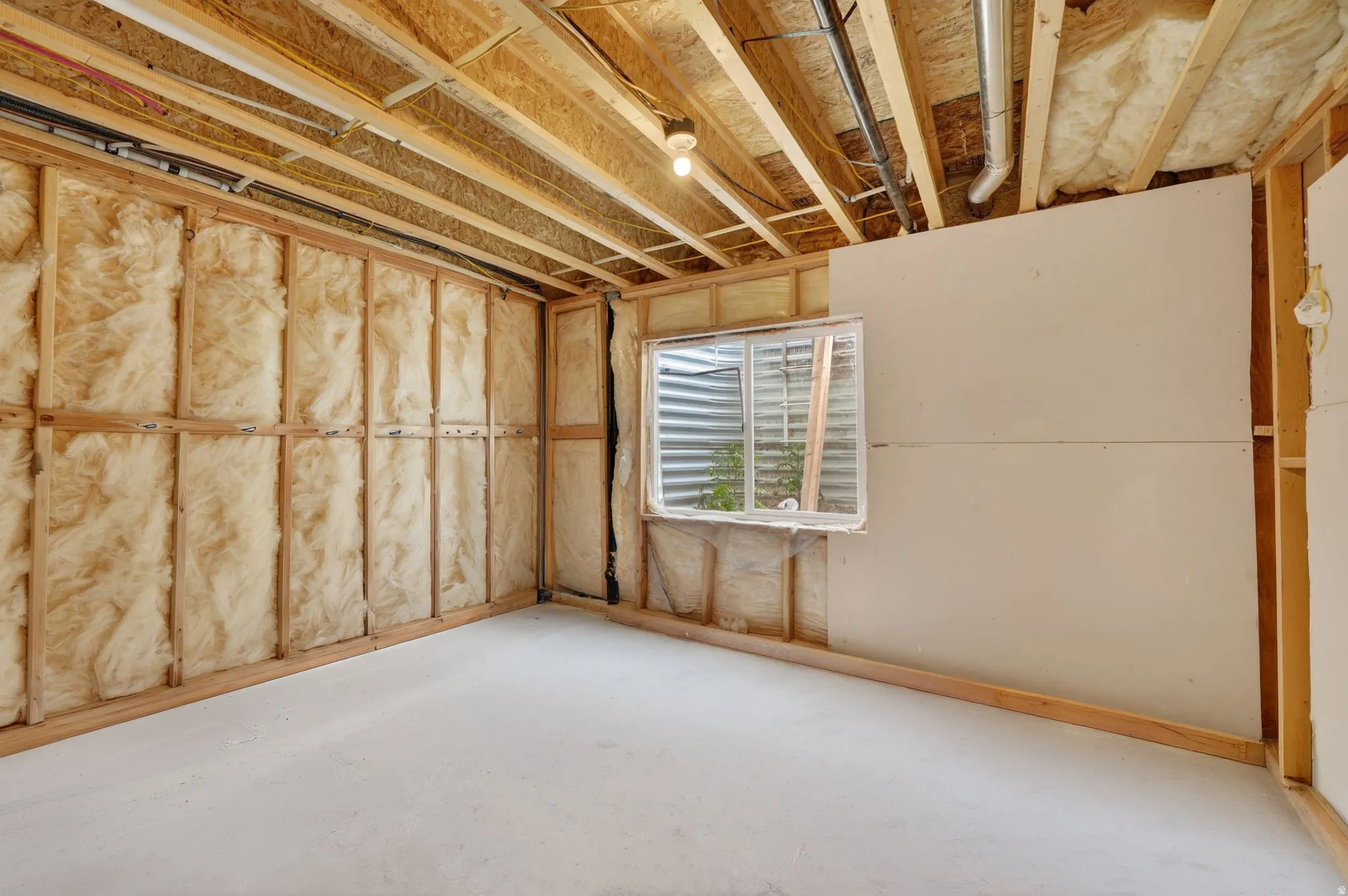 Unfinished basement space featuring exposed wood framing, insulation, and partial drywall installation