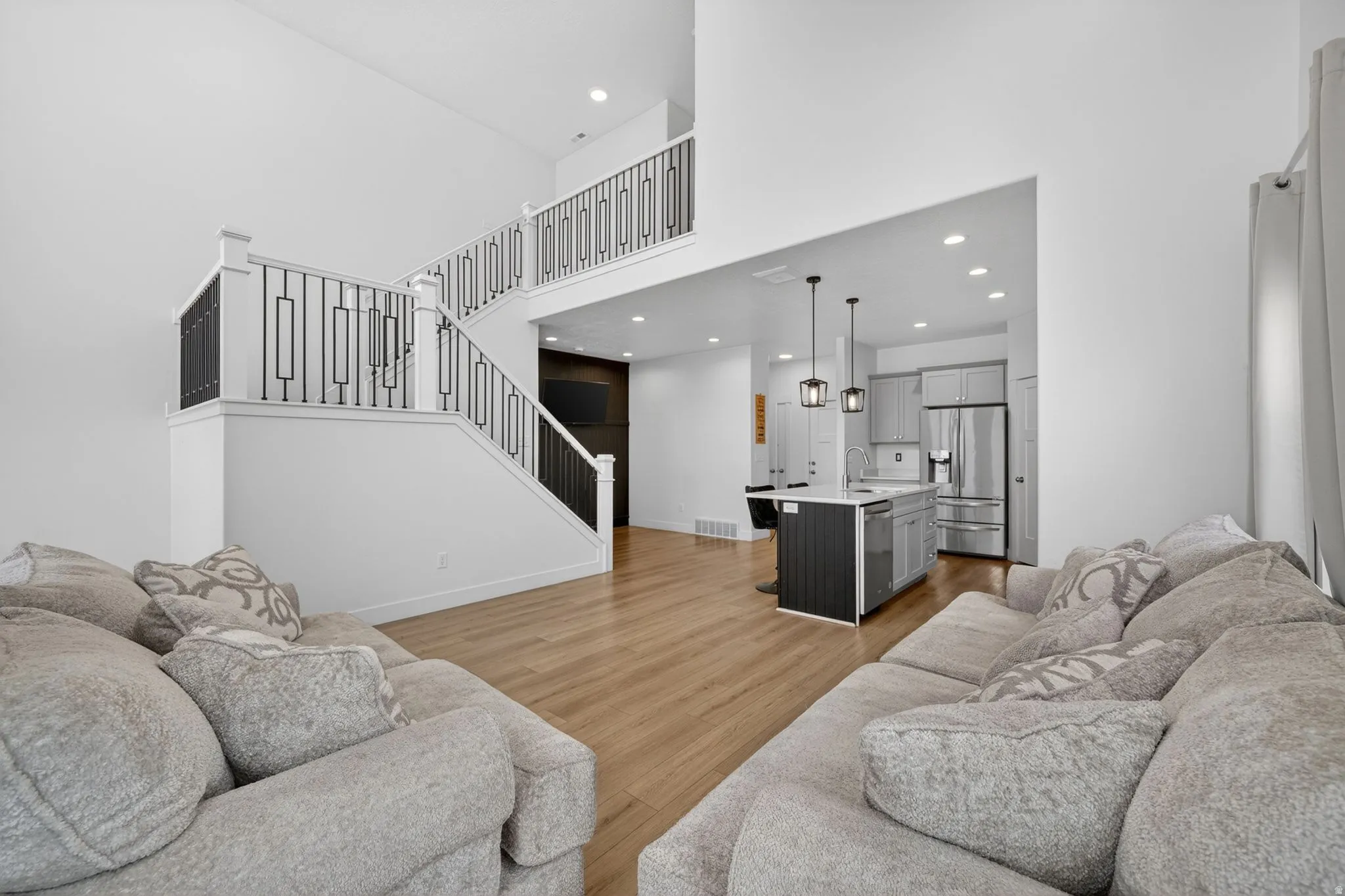 Open-concept living space featuring wood-finish flooring, a two-story ceiling, and a prominent staircase with metal balusters