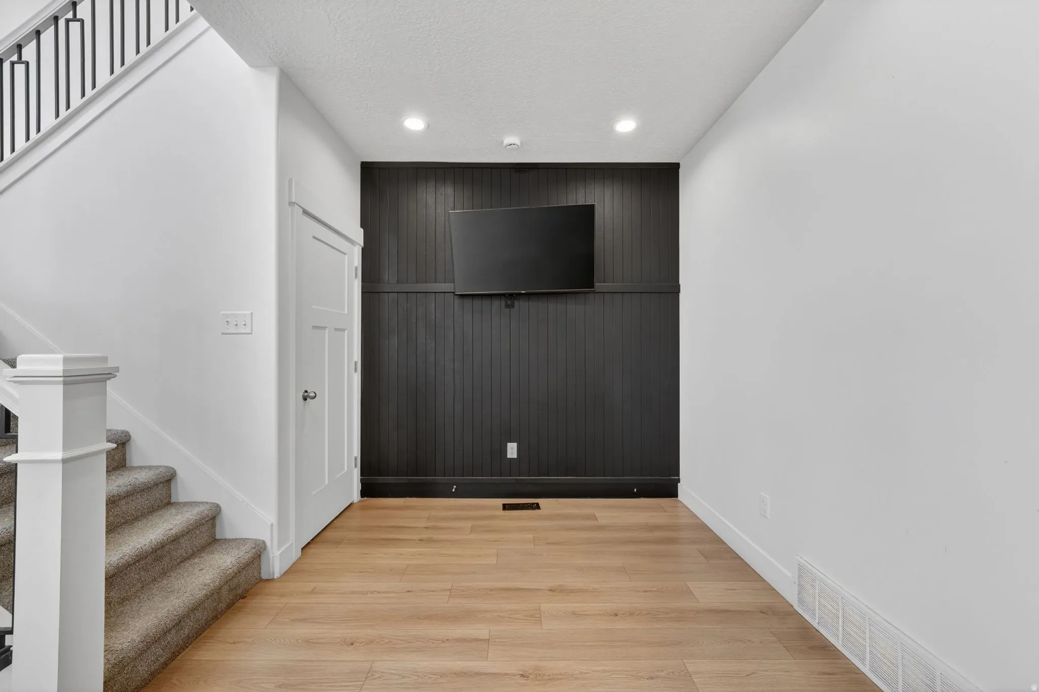 Inviting entry space featuring light wood-finish flooring and a contrasting dark paneled accent wall with recessed lighting