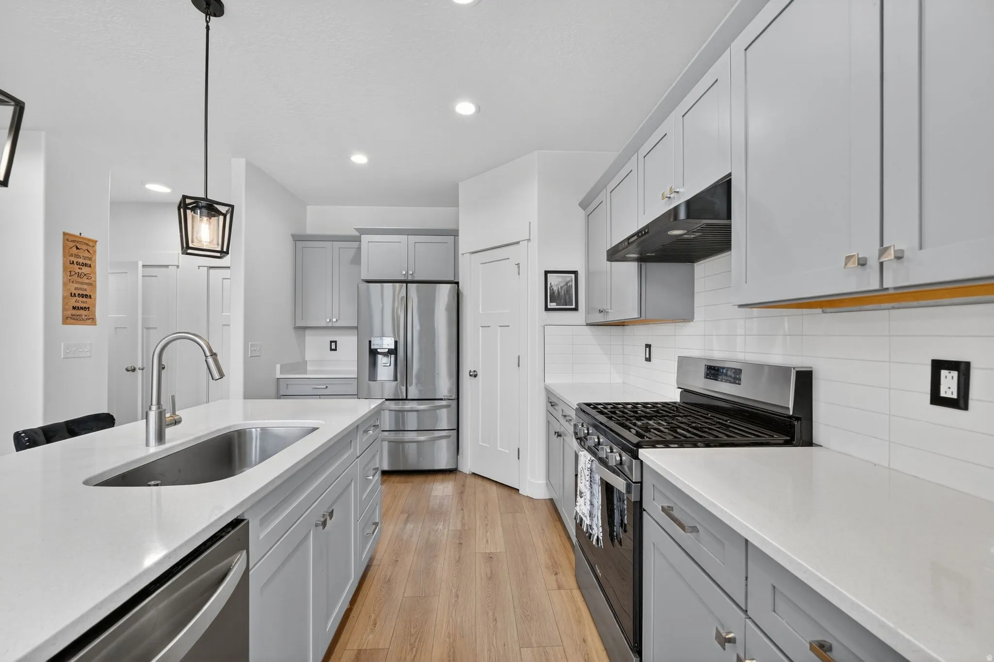 Kitchen featuring light wood-finish flooring, light gray cabinetry, white countertops, stainless steel appliances, and a white subway tile backsplash