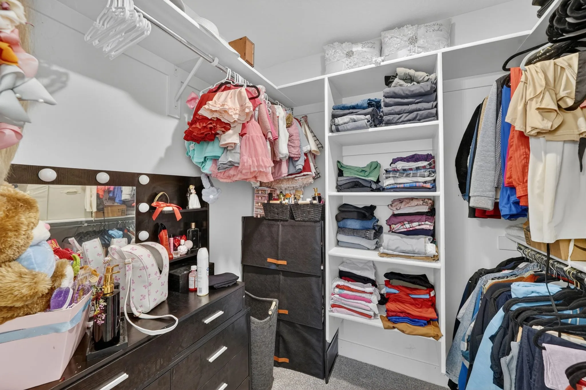 Walk-in closet featuring built-in shelving, hanging rods, an integrated vanity mirror with task lighting, and dark wood-finish cabinetry