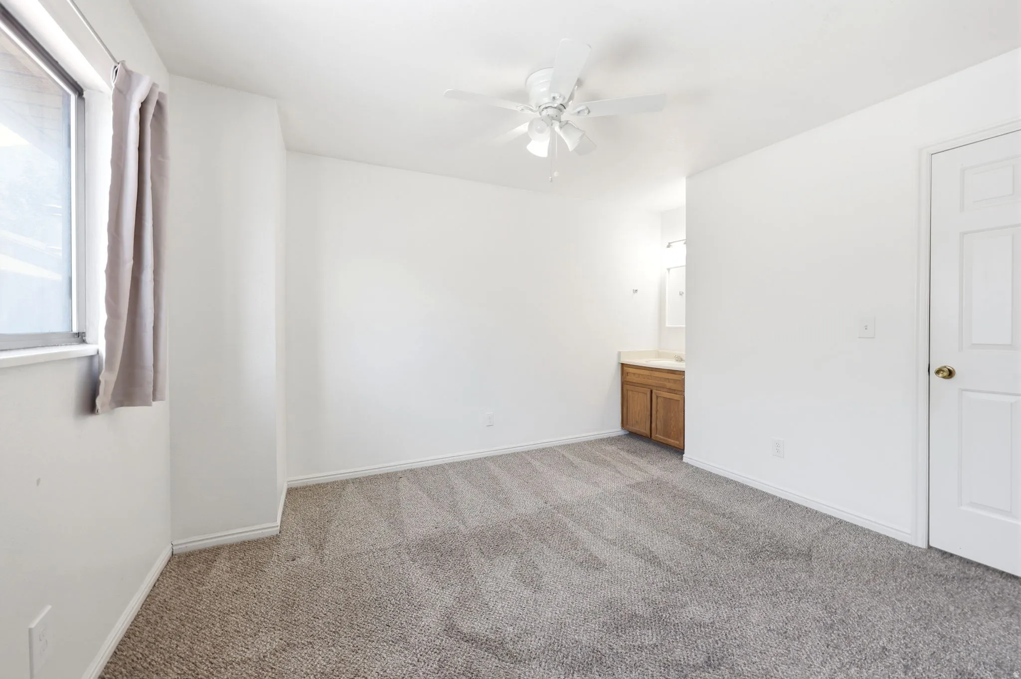 Carpeted bedroom featuring white walls, a ceiling fan, and a window with a light-filtering curtain