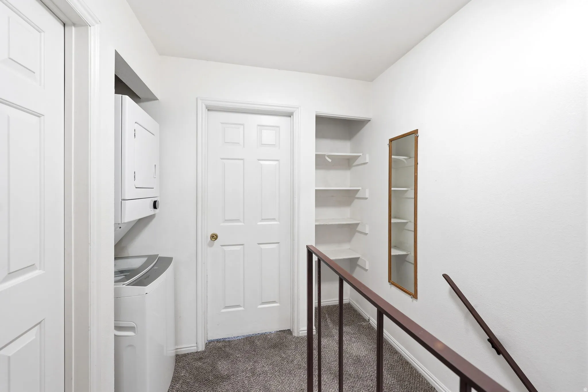 Integrated stacked washer and dryer unit, built-in shelving, white paneled doors, and dark carpeted flooring