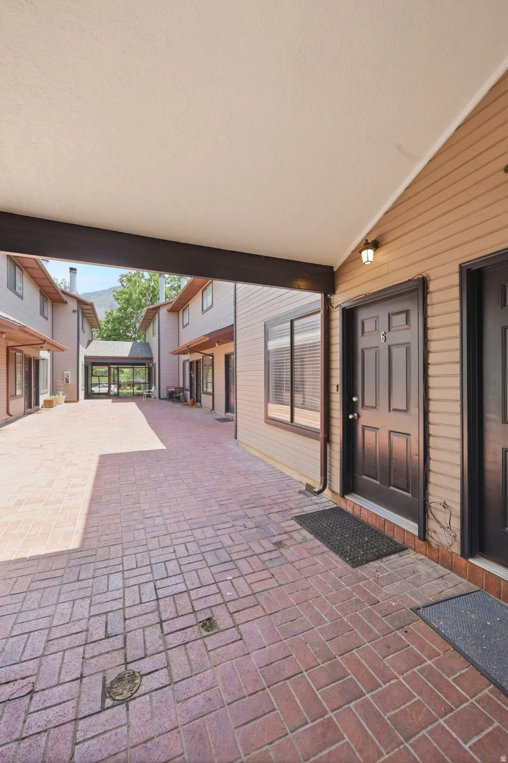 Brick paver courtyard with covered walkways, featuring wood-finish siding and dark entry doors with exterior lighting fixtures