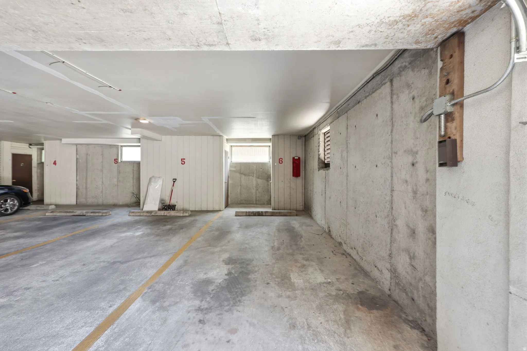 Concrete parking garage featuring designated parking spaces with painted lines, concrete walls, a painted concrete ceiling, and limited window openings