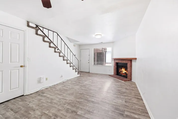 Living area featuring wood-finish flooring, a brick fireplace with a wood mantel, and a staircase with a metal railing