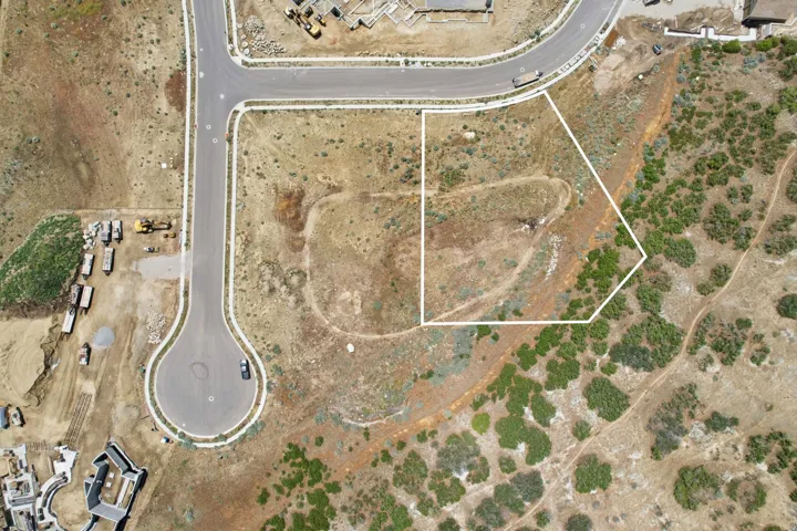 Expansive land parcel with defined boundaries, featuring varied terrain and natural vegetation, bordering a developed roadway