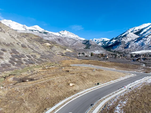 Paved roads and sidewalks define the property's edge, framed by undeveloped land and distant snow-capped mountains