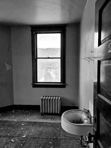 Room featuring a single-hung window with dark wood trim, a wall-mounted sink with dual faucets, and a cast-iron radiator