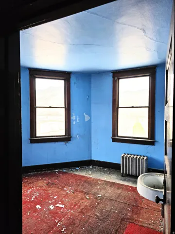 Room featuring two windows with dark wood trim, a wall-mounted sink, and a radiator
