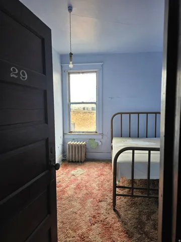 Interior room featuring a single window, a wall-mounted radiator, and an exposed bulb pendant light fixture