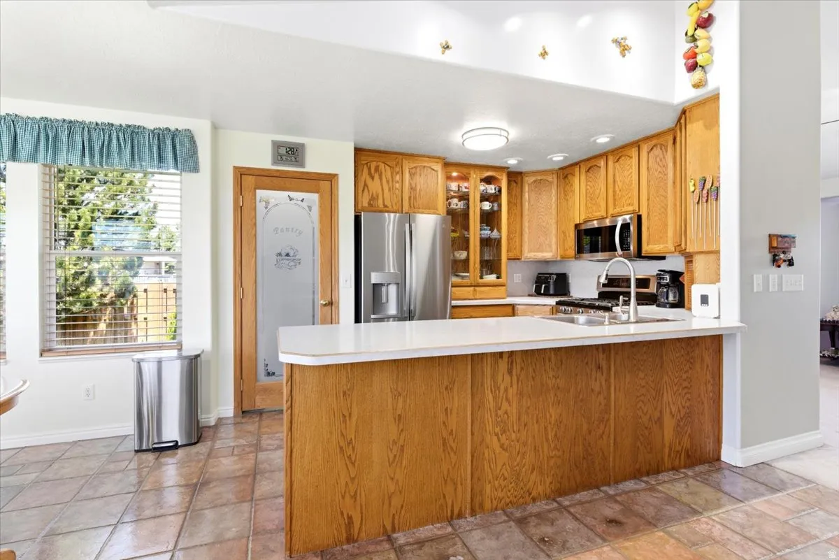 Kitchen featuring wood cabinetry, stainless steel appliances, a white countertop, and tile flooring