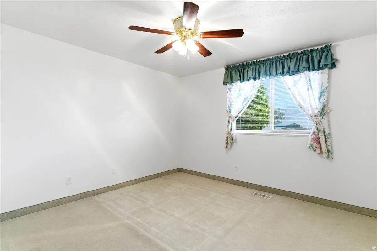 Carpeted room featuring a ceiling fan with light fixture, a window with blinds, and white walls