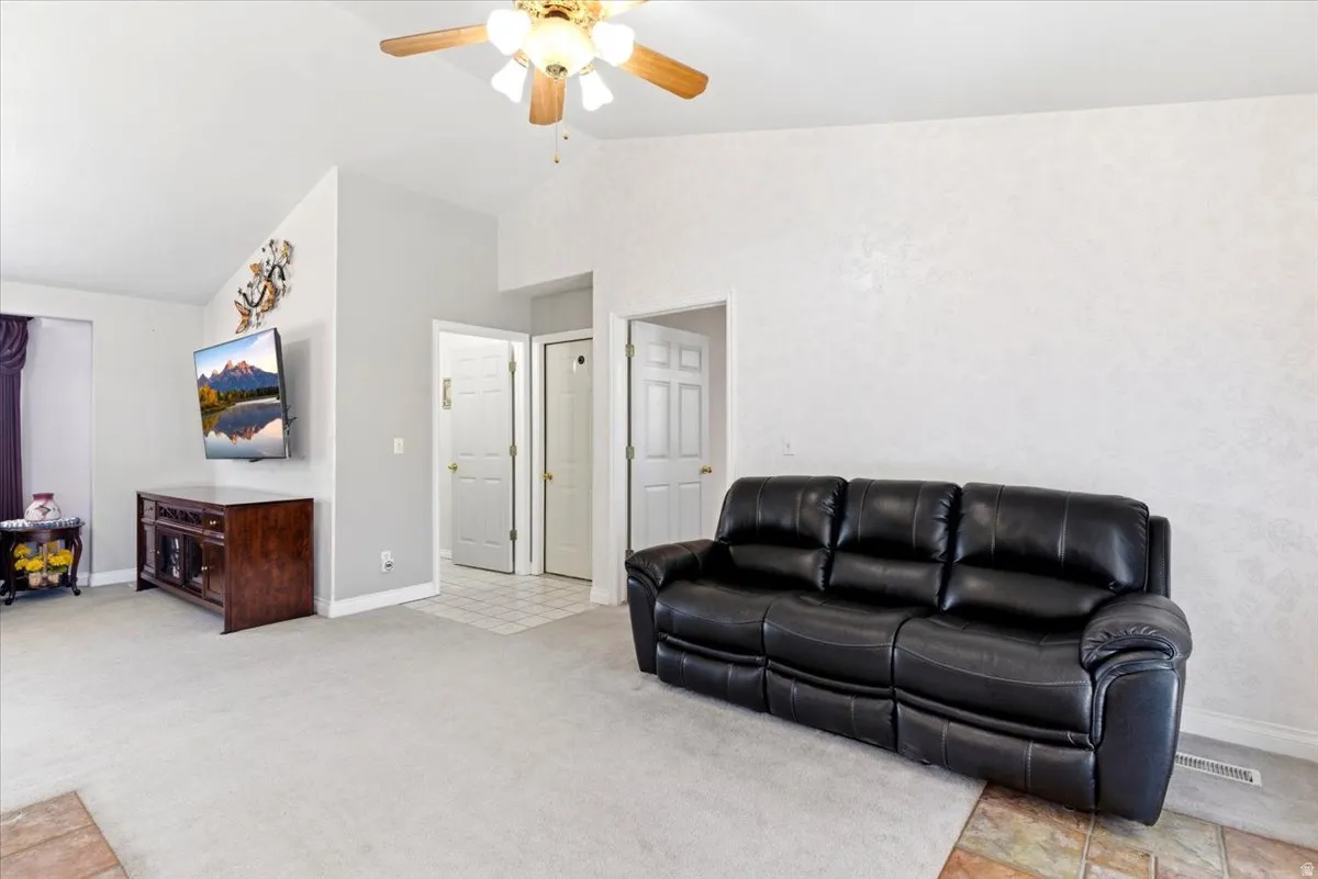 Vaulted ceilings with a ceiling fan light fixture, light-toned wall finishes, light-toned carpet flooring, and white baseboards