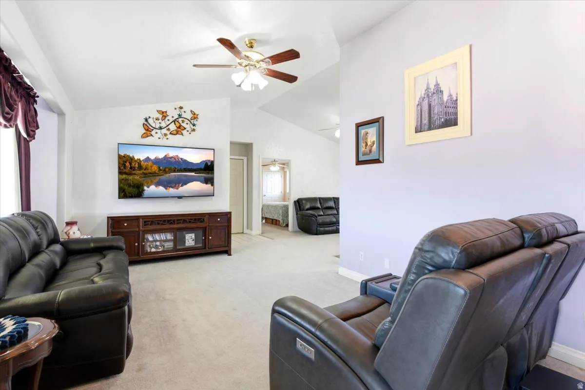 Living room featuring vaulted ceilings, ceiling fan, neutral wall colors, wall-mounted television, and wood-finish media console